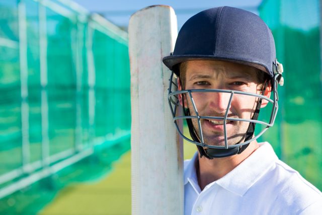 Cricket player wearing helmet holding bat at pitch, showing confidence and readiness for the game. Ideal for use in sports-related articles, advertisements for cricket gear, or promotional materials for cricket events and training programs.