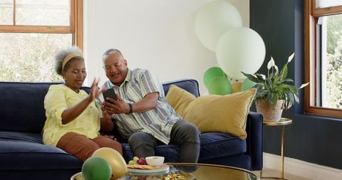 Joyful Senior Couple Celebrates with Balloons While Taking Selfie on Couch