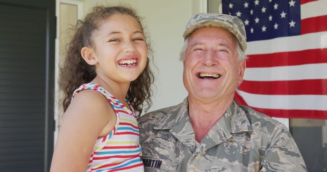 Image of happy caucasian senior soldier wearing uniform with granddaughter standing outside house. Patriotism, armed forces and family life.