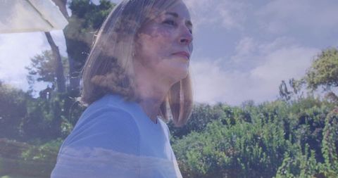 Mature woman gazing with dreamy cloud double exposure, contemplative outdoor portrait