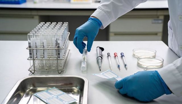 Lab technician labeling sample tube with gloved hands next to test tube rack