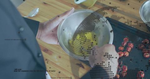 Straining silky egg yolk through fine sieve into stainless bowl with roasted cherry tomatoes