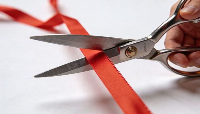 Cutting red satin ribbon with silver tailor scissors showing serrated zigzag edge