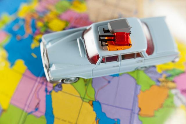 Miniature car with luggage on roof placed on a colorful world map. Ideal for travel blogs, vacation planning websites, travel agencies, and educational materials about geography and global exploration.