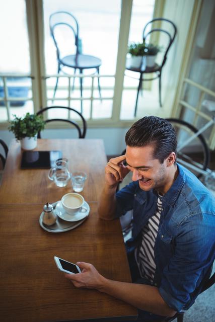 Smiling man using mobile phone with cup of coffee on table in cafÃ©