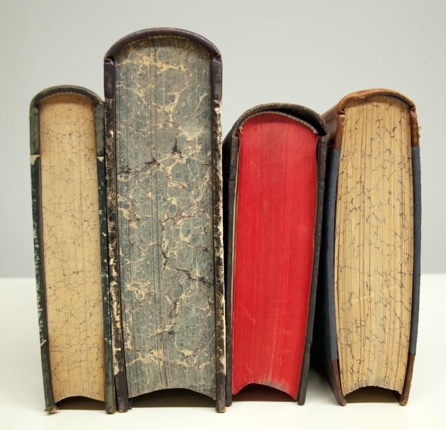 Close-up of four vintage books with worn spines and edges showcasing unique classic bookbinding. Ideal for concepts related to literature, history, and education. Perfect for illustrating antique books, cultural heritage preservation, and bibliophiles' interests.
