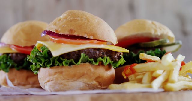 Three cheeseburgers with fresh toppings, lettuce, tomatoes, onions, cheese, and buns, next to a serving of crispy french fries. Ideal for use in advertisements for restaurants, fast-food chains, takeout menus, and food delivery services. Suitable for promoting food-related events, social media posts about meals, comfort food blogs, and culinary publications.