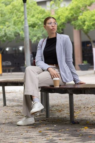 African american professional woman sitting on bench in urban plaza holding coffee
