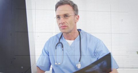 Focused male doctor reviewing digital records on monitor with tablet and stethoscope
