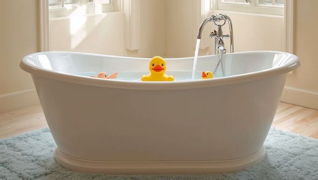 Freestanding white bathtub featuring floating rubber ducks in sunlit bathroom