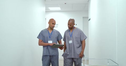 Two african american radiology technologists reviewing tablet in modern hospital corridor