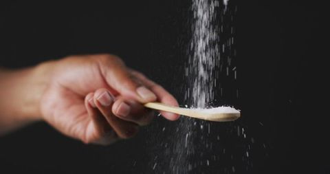 Hand sprinkling salt with wooden spoon in kitchen close-up