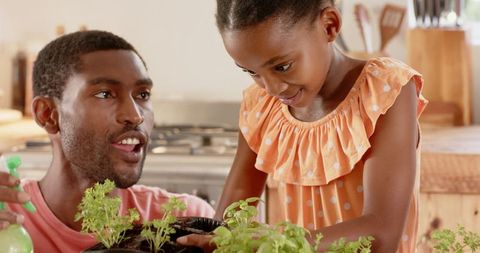 Smiling father and daughter watering kitchen herb garden