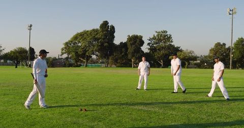 Amateur cricket teammates standing on green field wearing whites with bat and red balls