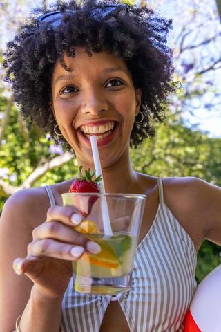 Joyful african american woman smiling and holding citrus drink outdoors in striped top