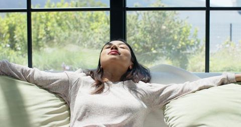 Relaxed woman reclining on sofa bathed in sunlight through black-framed window