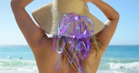 Blonde woman wearing straw sunhat at beach with iridescent jellyfish projection