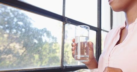 Person Hydrating Near Window with Morning Sunshine