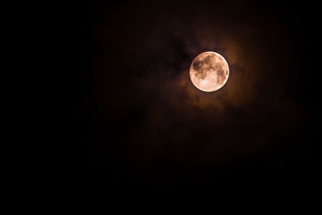 The full moon emerges through the dark clouds in night sky, creating an eerie and captivating atmosphere. Suitable for use in astronomy blogs, nature websites, atmospheric mood settings in media, supernatural or cosmic-themed projects, and desktop wallpapers.