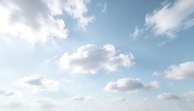 Soft cumulus clouds drifting across clear blue sky with warm sun glare and open horizon