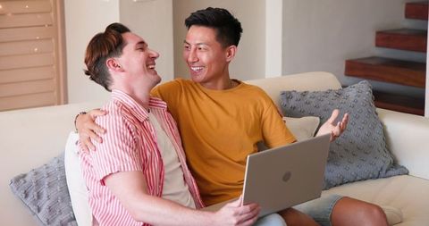 Happy Diverse Gay Couple Enjoying Technology Together on Couch