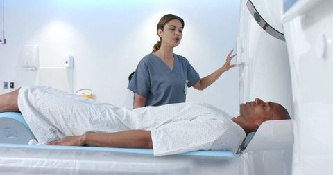 African american man lying on ct table, female technologist operating gantry
