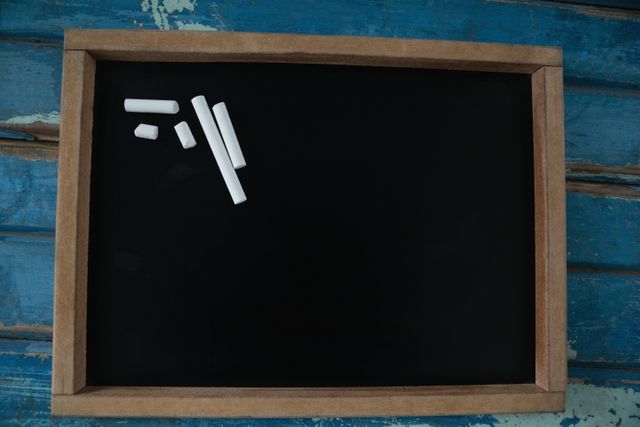 Blank slate with chalk pieces on a blue wooden background. Ideal for educational themes, school-related content, teaching materials, and learning concepts. Can be used for presentations, blog posts, and social media graphics related to education and classroom activities.
