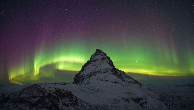 Glowing aurora dancing above snowcapped pyramidal peak under starry arctic night sky