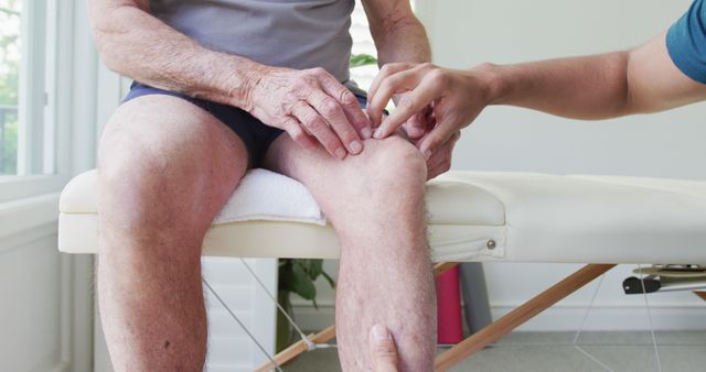Elderly man sitting on treatment table while therapist giving knee massage. Great for illustrating rehabilitation services, elderly healthcare, and injury recovery treatments. Suitable for use in health and fitness articles, medical brochures, and physical therapy websites.