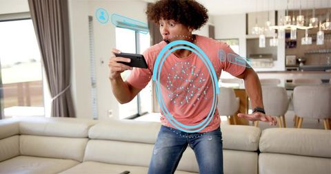 Young man reacting to augmented reality mobile game with interactive ar rings in living room