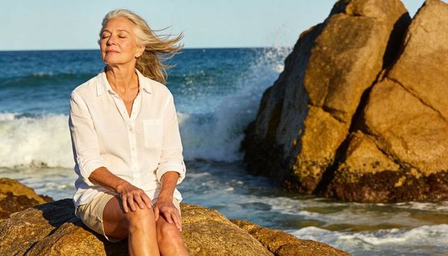 Senior woman enjoying ocean breeze on coastal rocks at golden hour