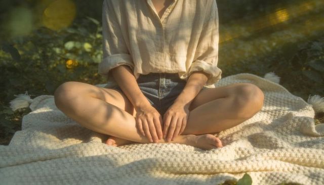 Sunlit woman sitting cross-legged on waffle-knit blanket meditating in tranquil garden