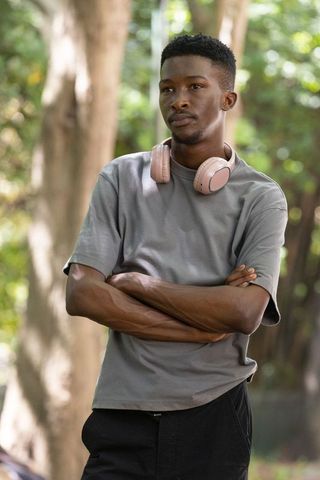 African man standing arms crossed wearing pink headphones gray tee outdoors