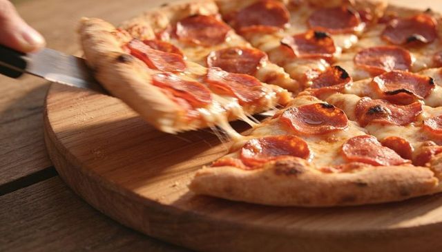 Pulling pepperoni pizza slice with stretching cheese on rustic wooden serving board