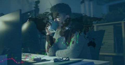 Working late analyzing global market data on desktop while sipping coffee wearing headset