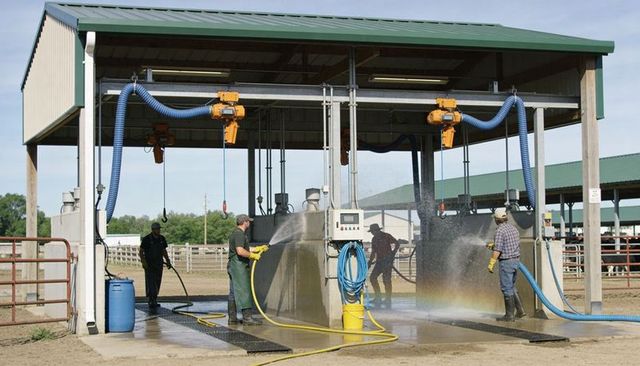 Farm workers washing livestock wash bay with hoses, creating rainbow under metal shelter