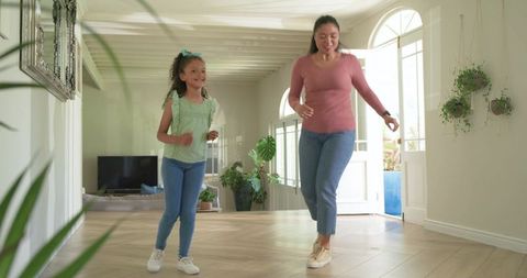 Mother and daughter walking and laughing on parquet floor in bright plant-filled hallway