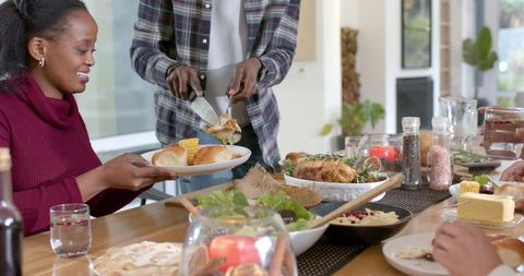 African American couple sharing holiday dinner while man carves roasted chicken at table