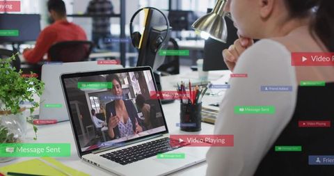Watching colleague during video conference on laptop in open-plan office with UI overlays