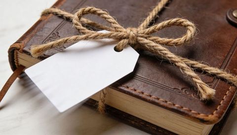 Rustic leather journal wrapped in jute twine with blank gift tag on marble surface