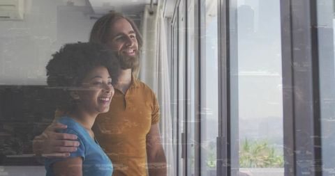Couple embracing and gazing through floor-to-ceiling doors at urban skyline view