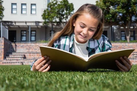 Young Girl Enjoying Outdoor Reading on School Campus Lawn
