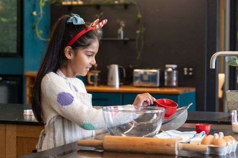 Young asian girl measuring ingredients with red cup and mixing in bowl in cozy kitchen