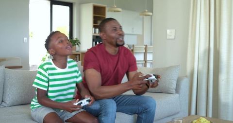 African American Father and Son Playing Video Games on Couch Sharing Laughter and Snacks