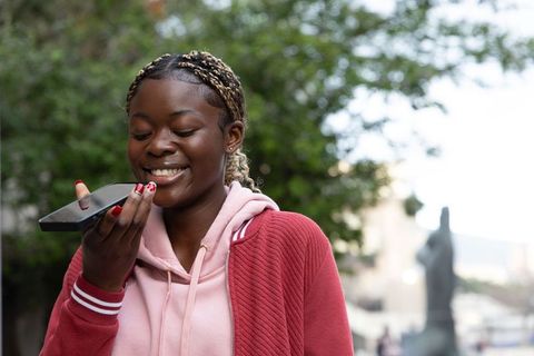 Smiling african american teen speaking into smartphone in urban plaza wearing pink hoodie