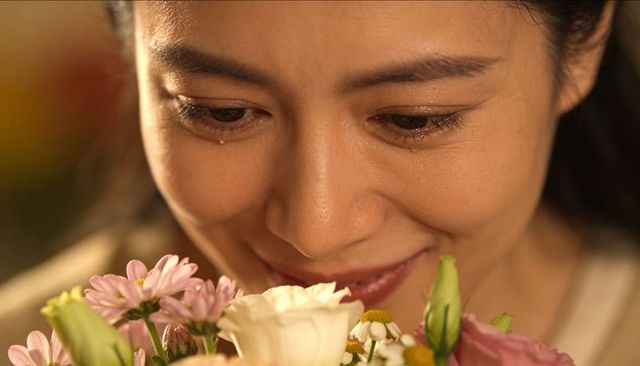Tearful asian woman smelling bouquet with gentle smile intimate floral closeup portrait
