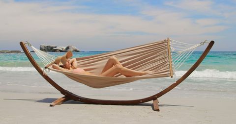 Woman Relaxing on Hammock at Tranquil Beach with Serene Blue Sky and Sea