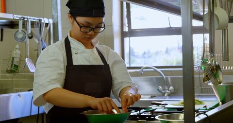 Focused Asian Female Chef Cooking in Professional Kitchen