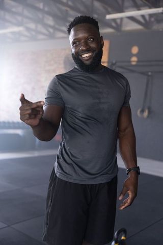 Smiling african american fitness coach pointing in industrial gym with kettlebell, bearded