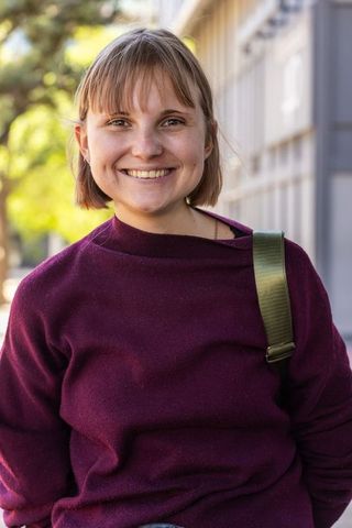 Young woman smiling on urban sidewalk wearing maroon sweater and green backpack strap